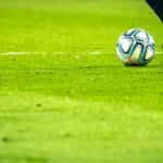 A ball and a pair of soccer player’s legs and shoes on grass.