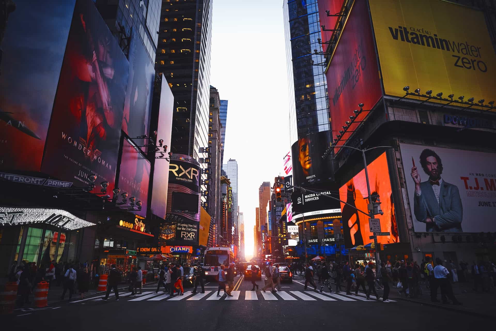A side street just off of Times Square in central Manhattan, New York City, with a sunset gleaming in the distance between rows of skyscrapers.